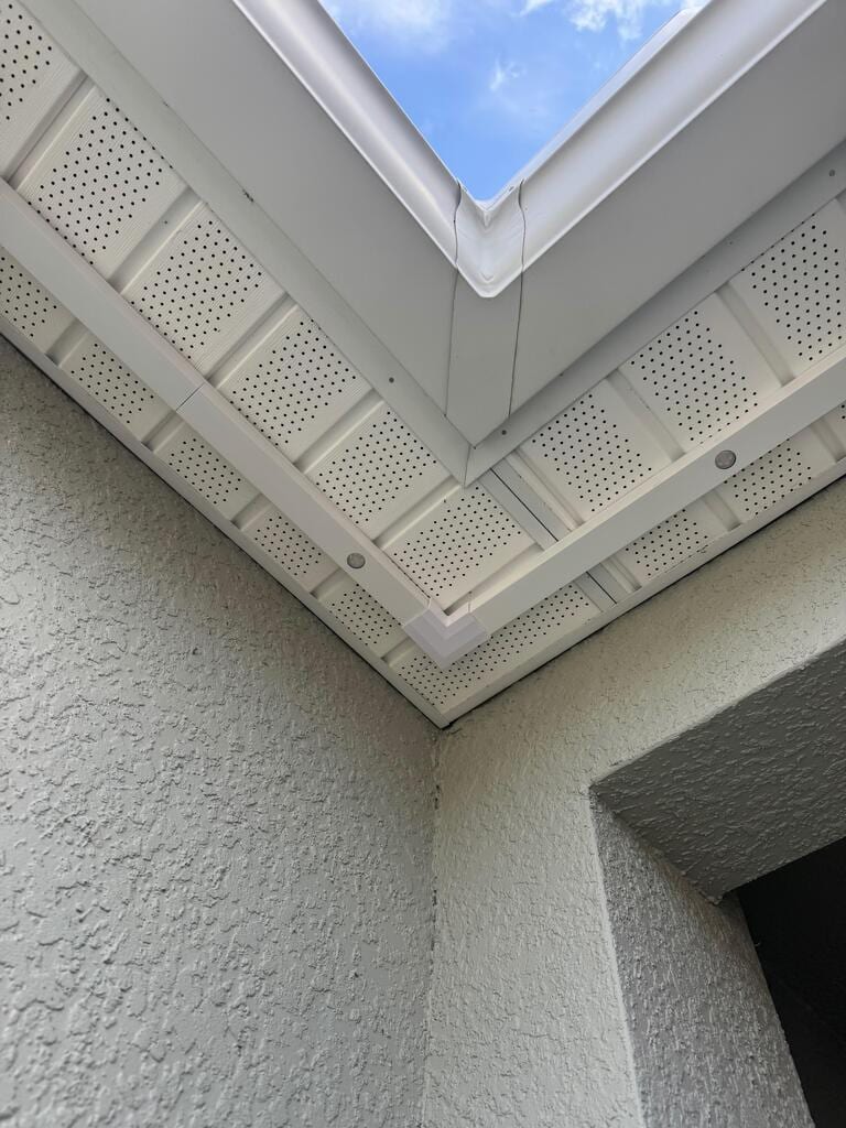 Daylight view of a stucco home corner showing the aluminum channel installed under the fascia. The channel is barely visible against the white perforated soffit.