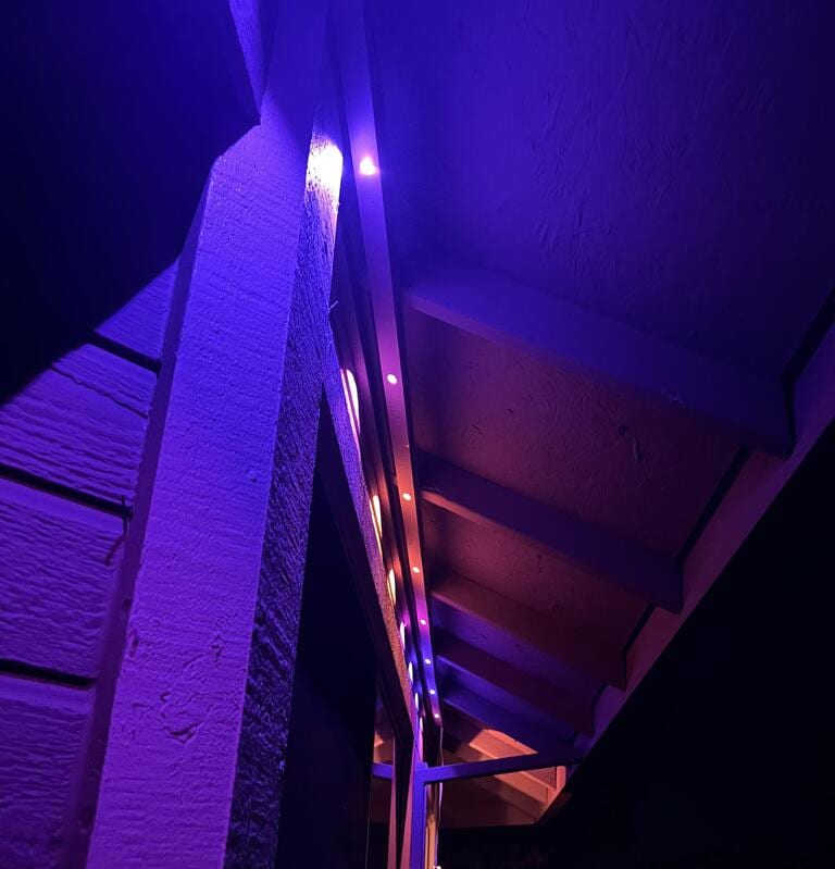 Nighttime view of a home's roofline lit in a purple-to-red color gradient using the permanent lights system, showing the individually addressable LED capability.