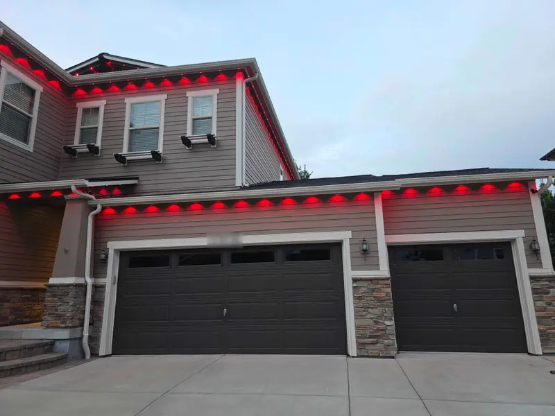 Two-story home in Denver Metro at dusk with Govee Pro permanent lights in SnapTrack glowing solid red along the roofline and above the garage