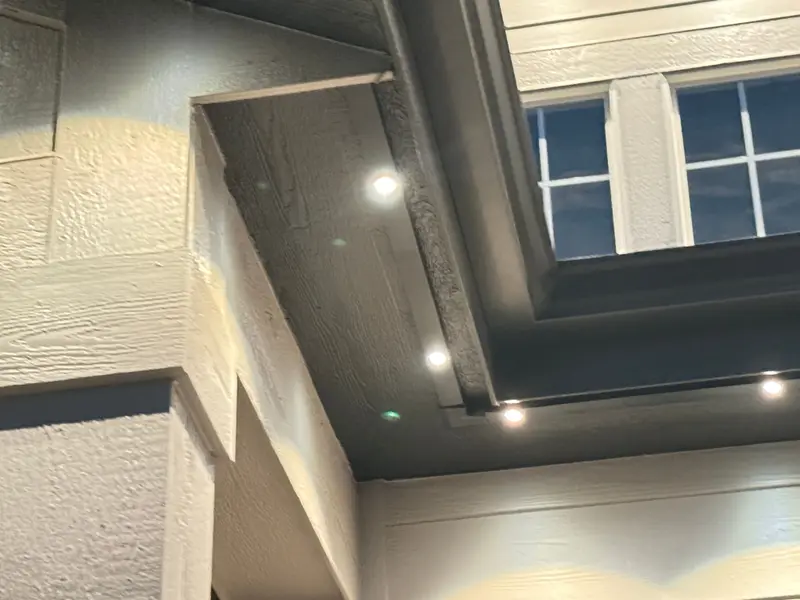 Close-up of aluminum SnapTrack mounted under a soffit with Govee Pro permanent lights glowing warm white, wiring fully concealed