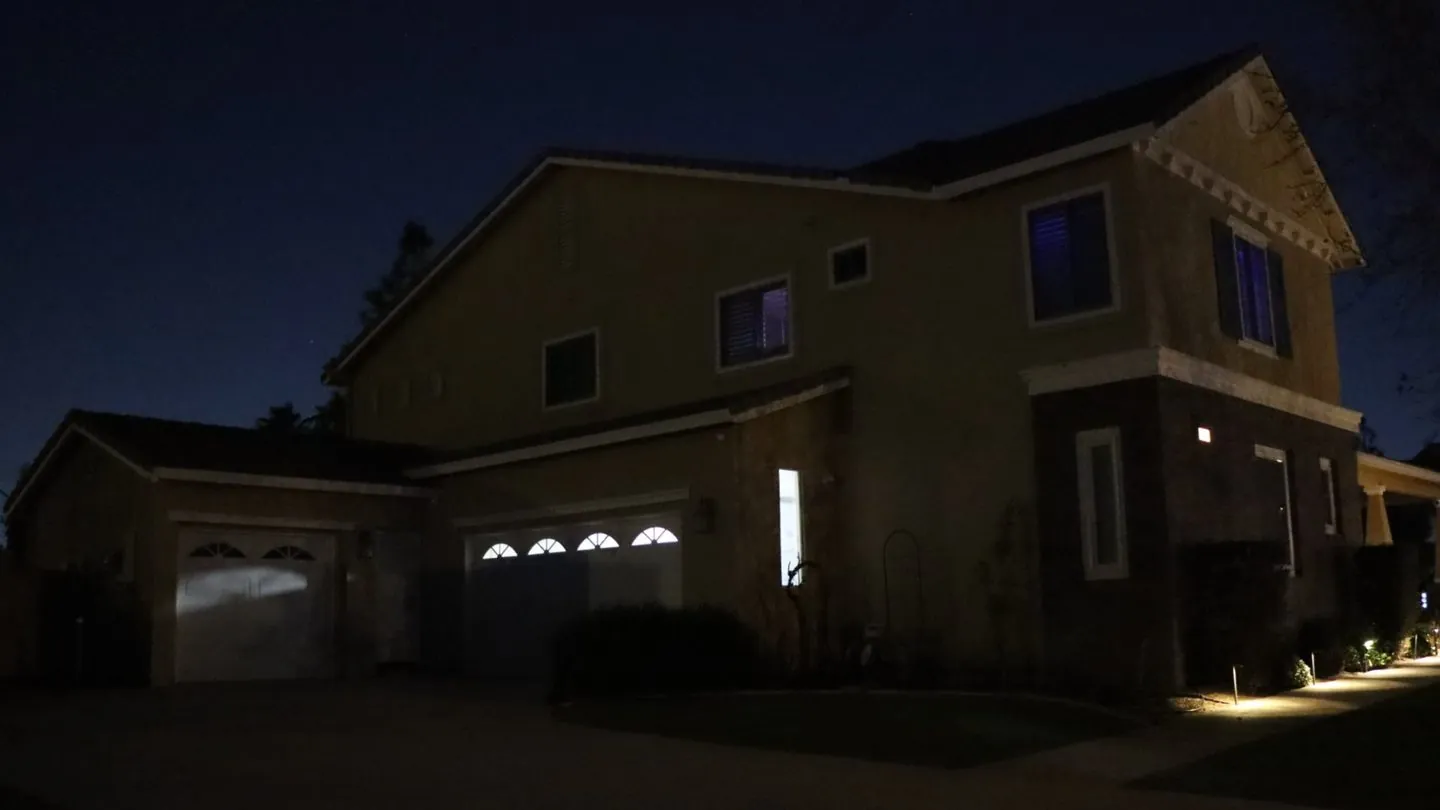 The same two-story home at night before permanent lighting, with a dark roofline