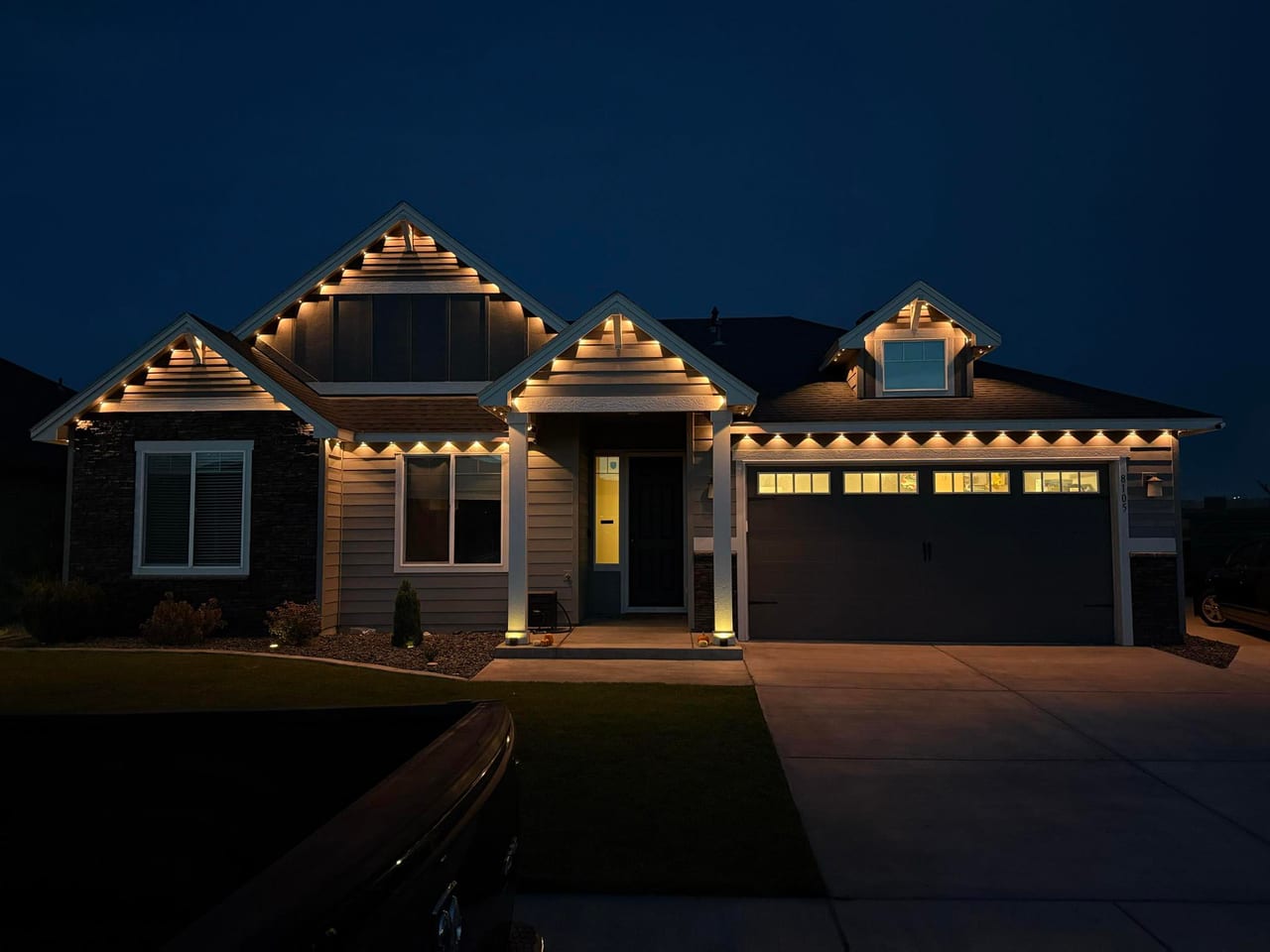 Warm white permanent outdoor lighting installed under the eaves and gables of a Denver Metro craftsman home at dusk